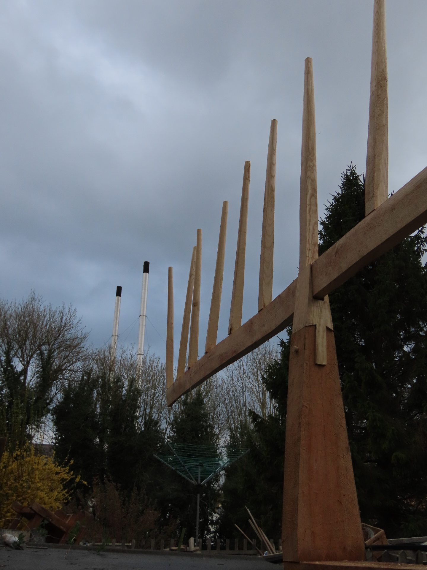 A heavily tined lop-sided sculpture aligned with two industrial chimneys.