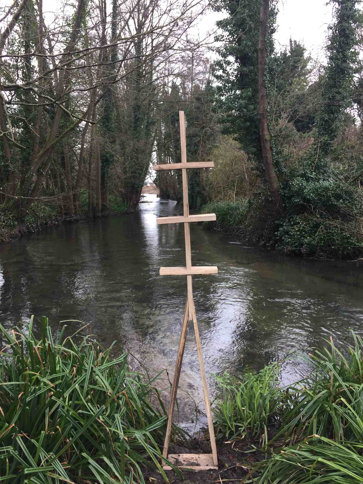 A Closer view of a plank based sculpture sat on a river bank.