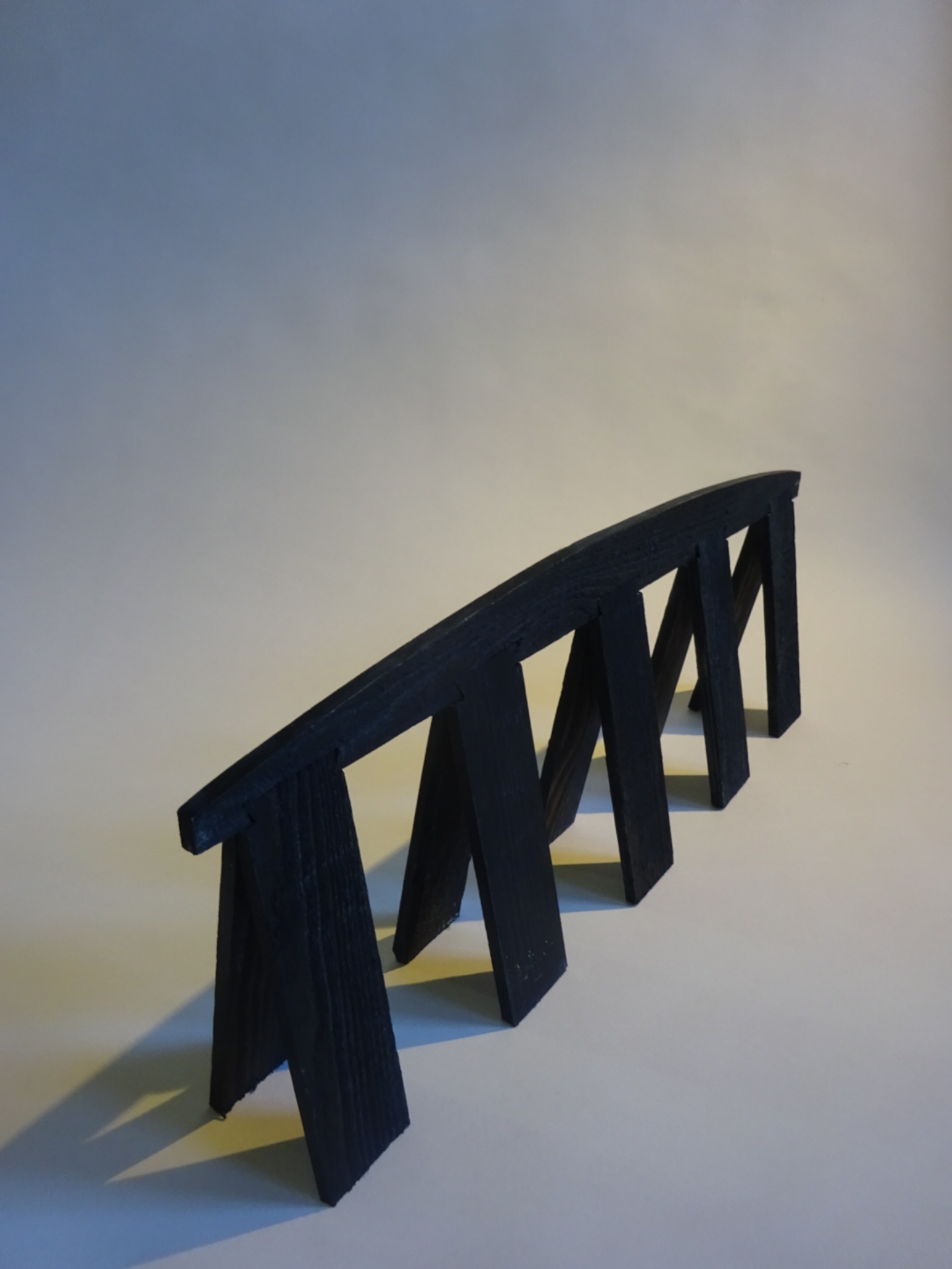 Painted wooden sculpture of a plank, curved across its spine and held up by ten legs dovetailed into its underbelly.