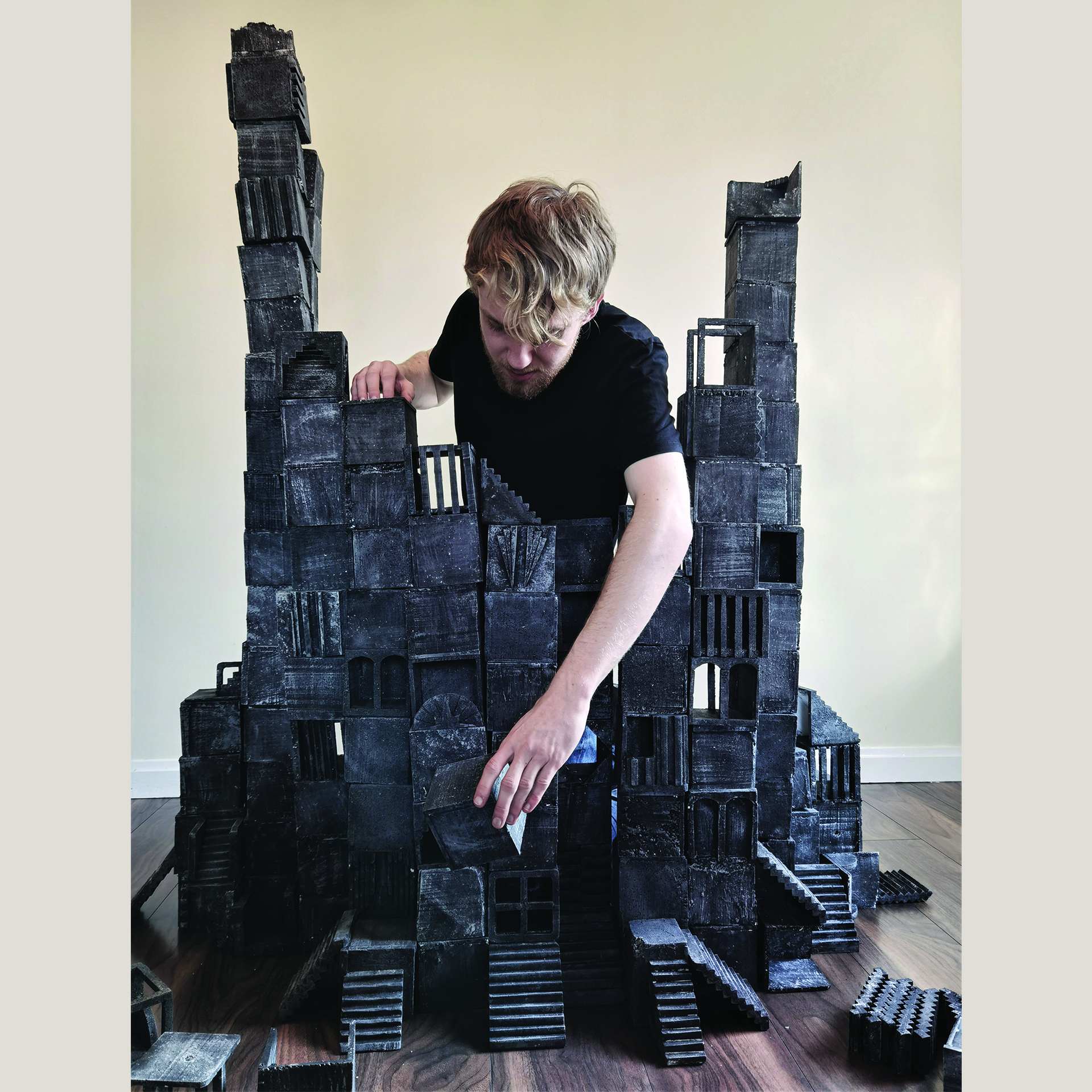 A person indoors, building a structure from grey blocks.