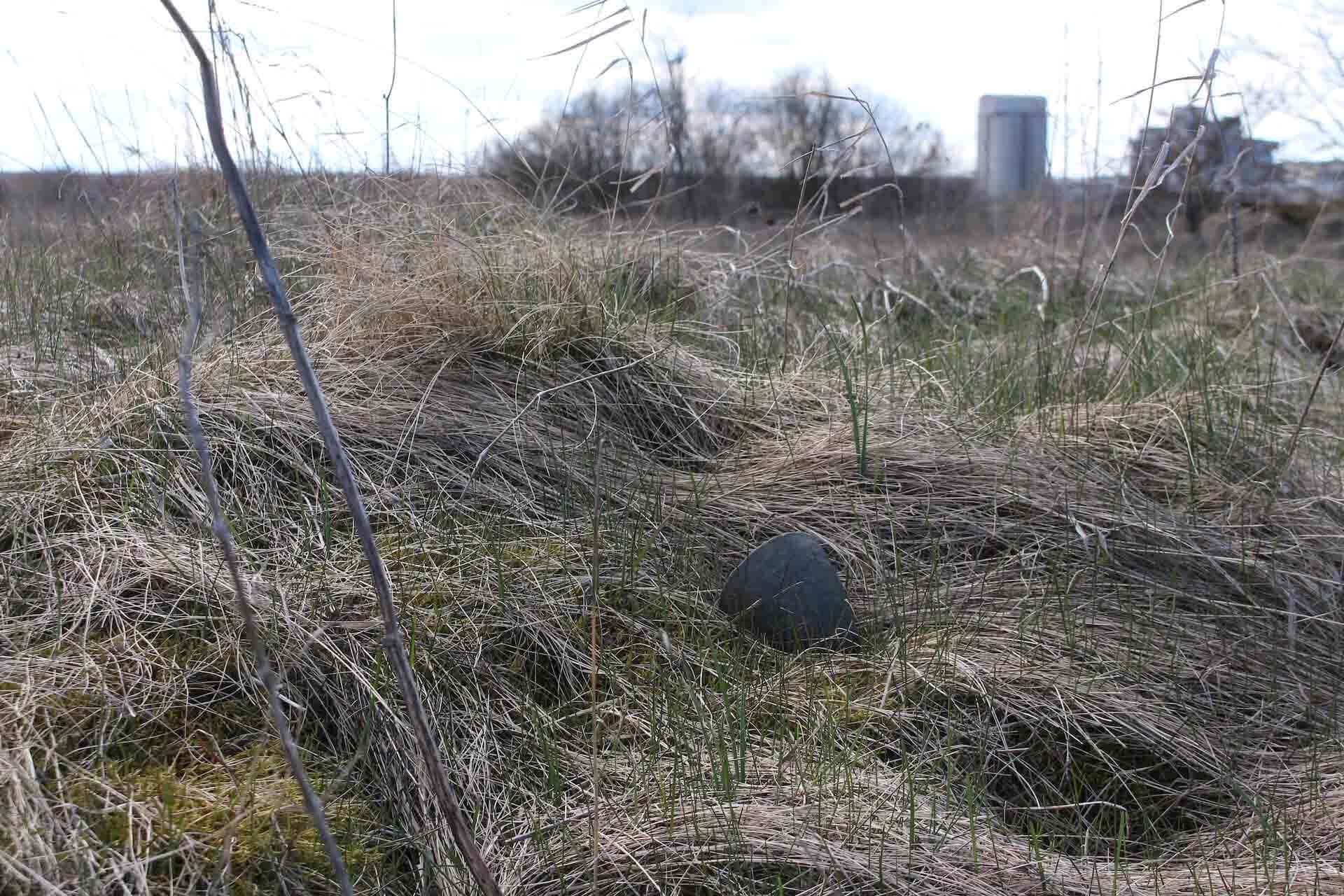 A small unfired green pot nestled in the grass.