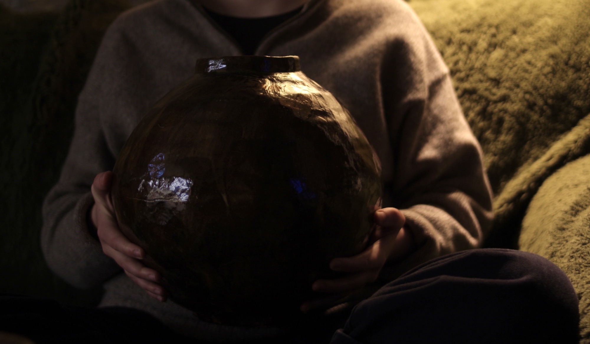 A large brown moon jar held in the artist's hands.