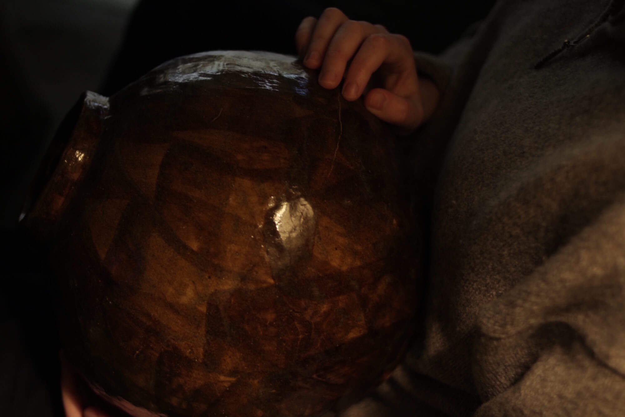 A large brown moon jar held in the artist's hands showing details of the glaze and small crack.