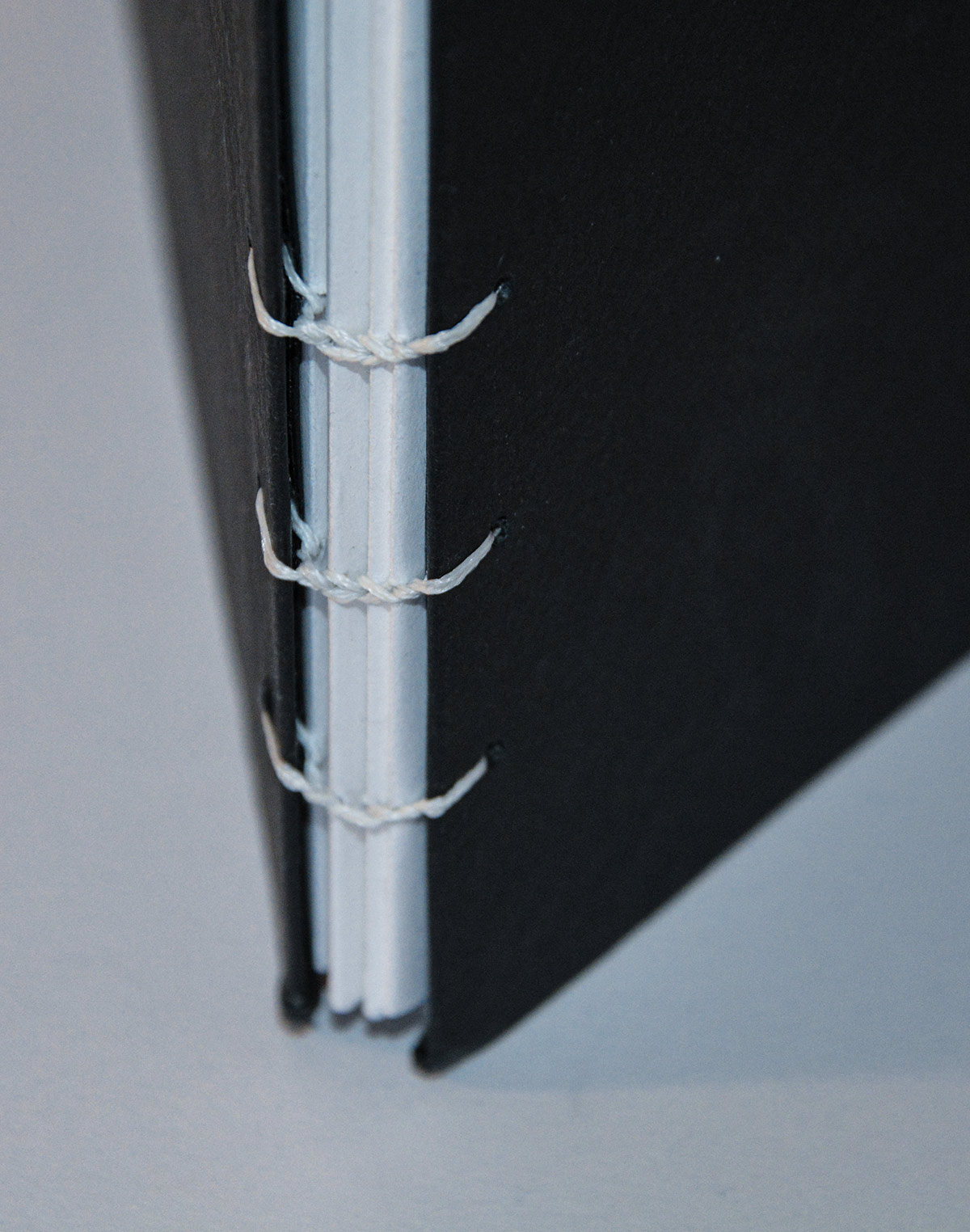 Close up of the bottom three rows of hand stitching book binding. White stitching creates a braid pattern, attched to the black covers.