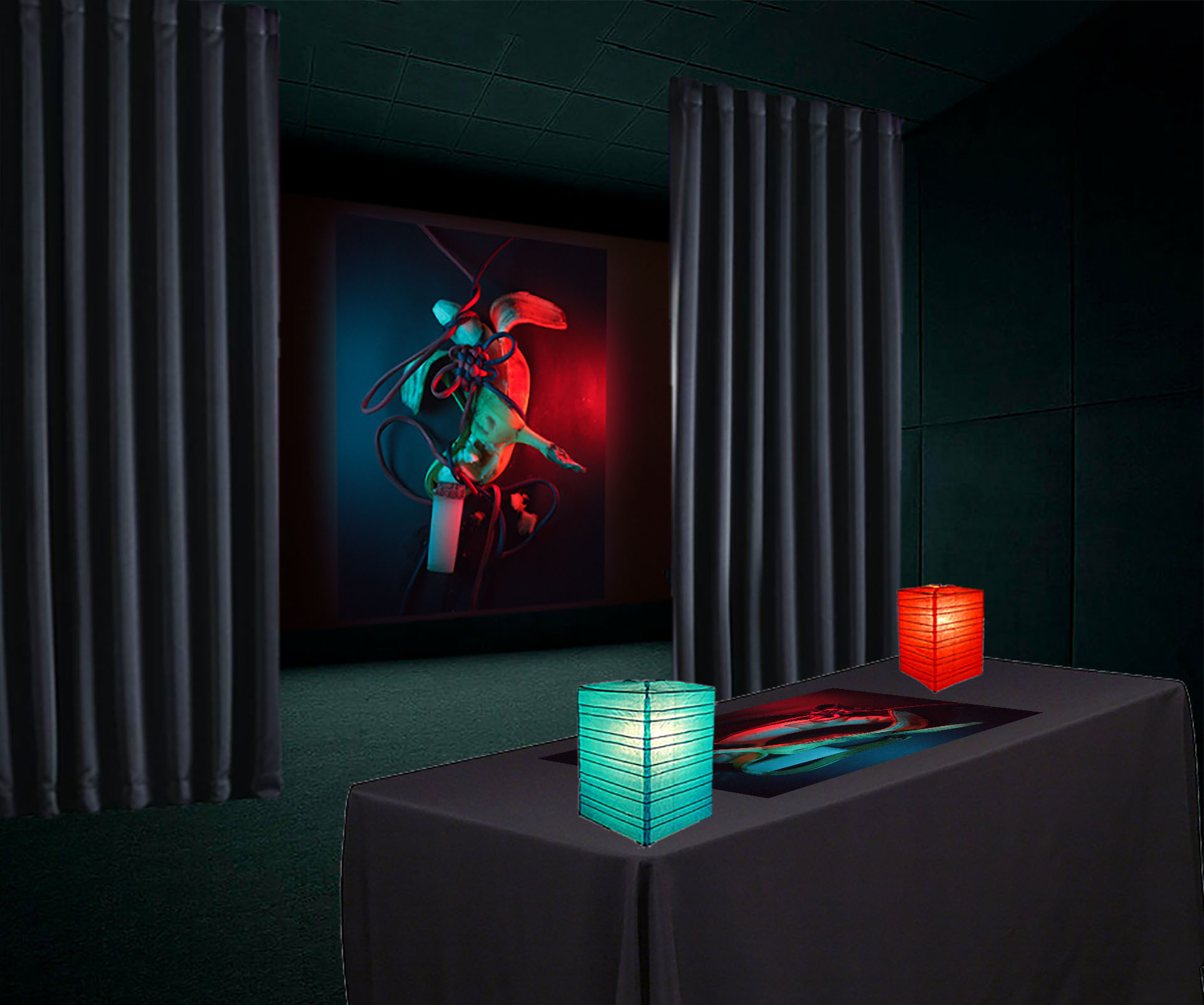 Projection of 'The Ritual of Kù’er Líng' behind curtains with a table in front. A black cloth covers the table and on the table is a physical recreation of 'The Ritual of Kù’er Líng' with red and blue lanterns.