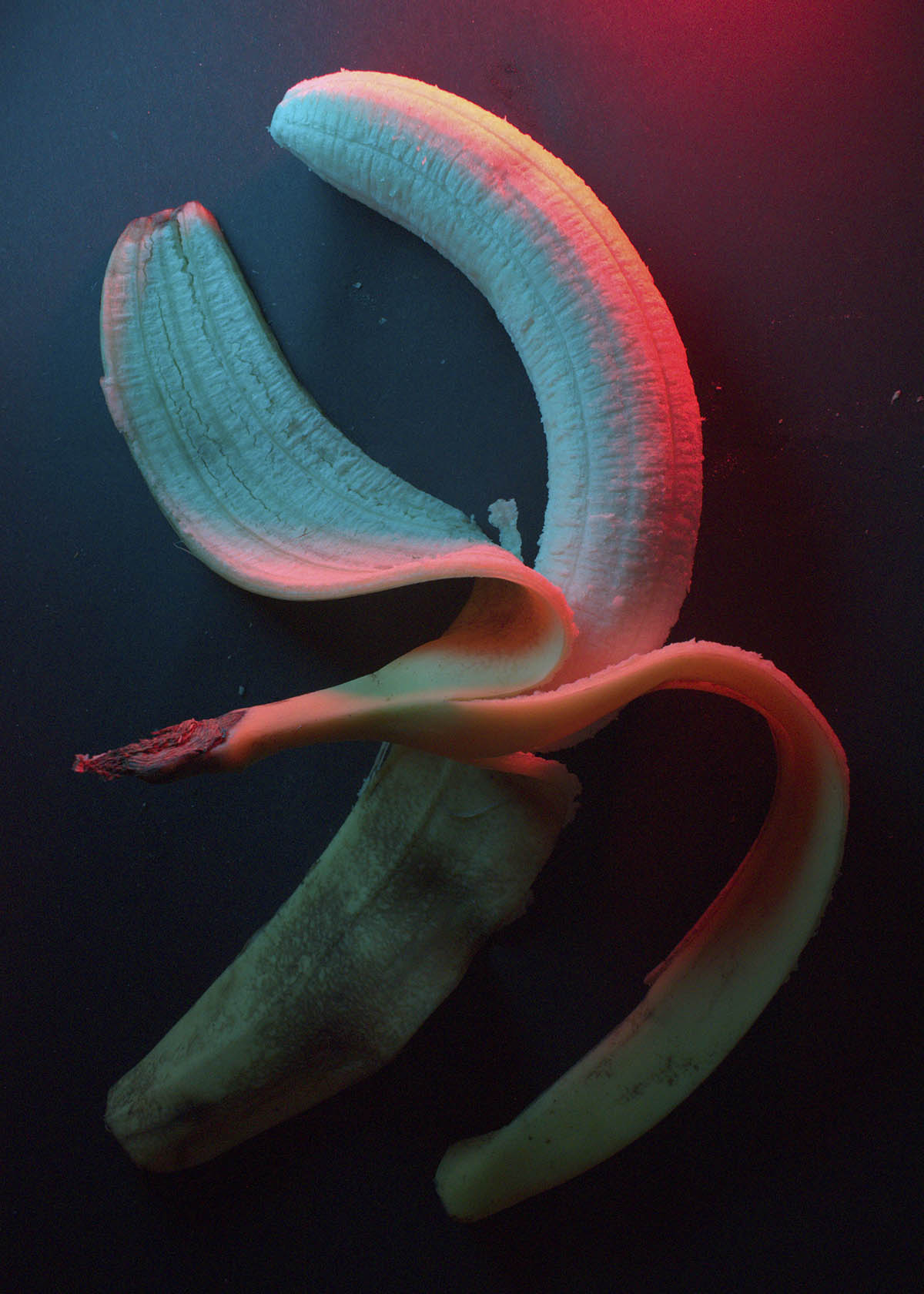 A peeled banana with the peel laying over one tip of the banana over a black background.