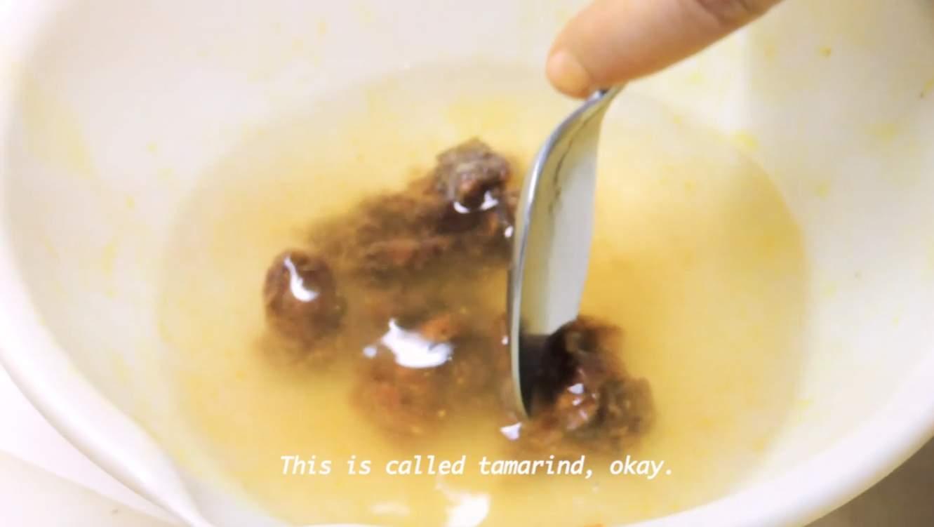 Video still of 'Visual Recipe' with translated subtitles, close-up of tamarind pulp diluted in water.