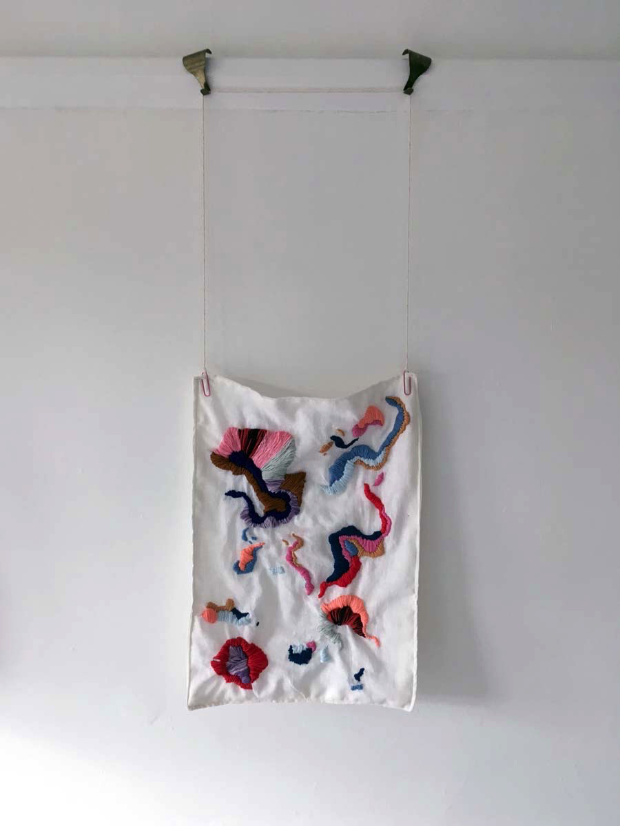White rectangle of fabric with embroidered multicoloured islands, hung on wall