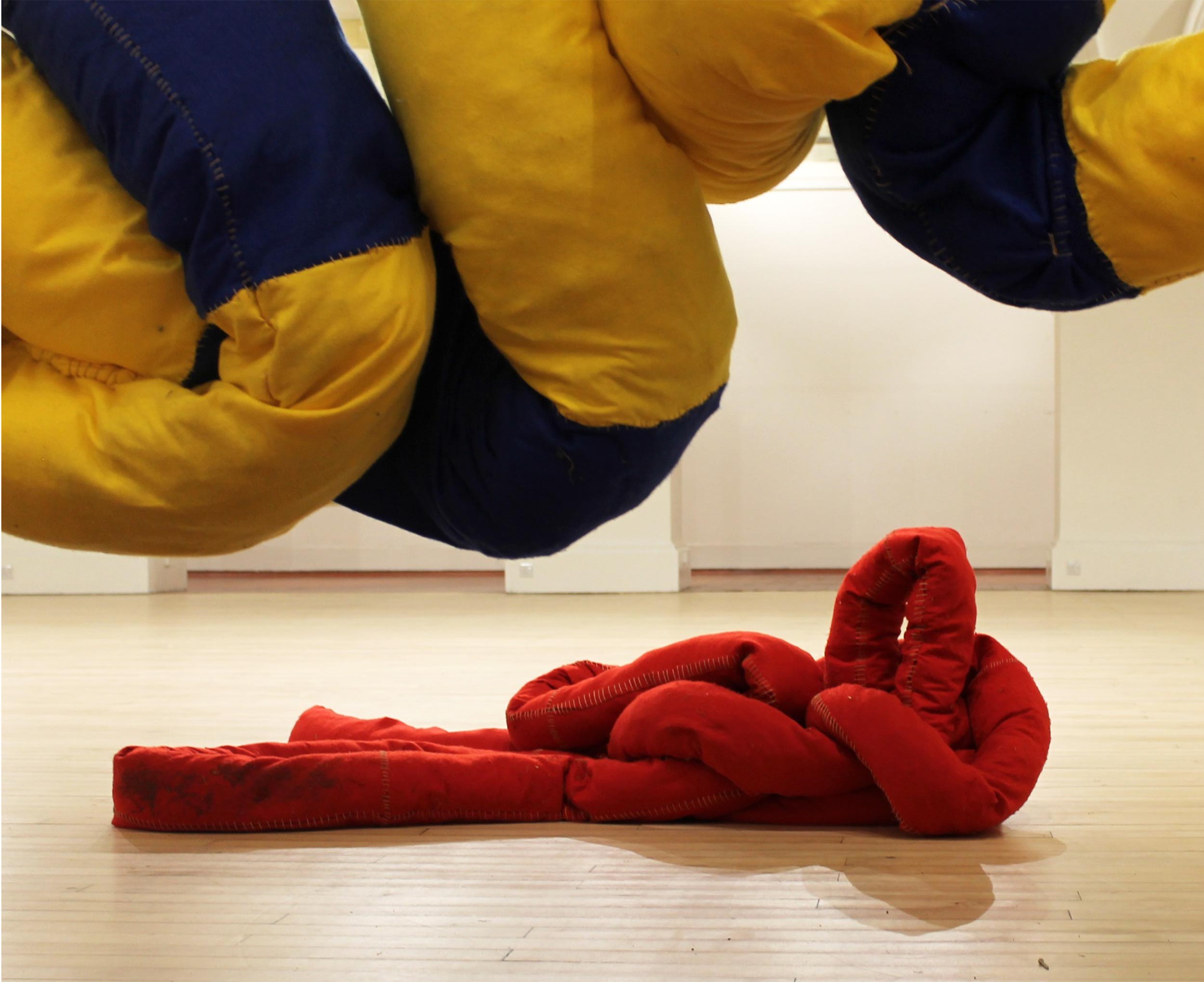 Two soft sculptures: blue and yellow suspended in the air, red situated on the ground. 