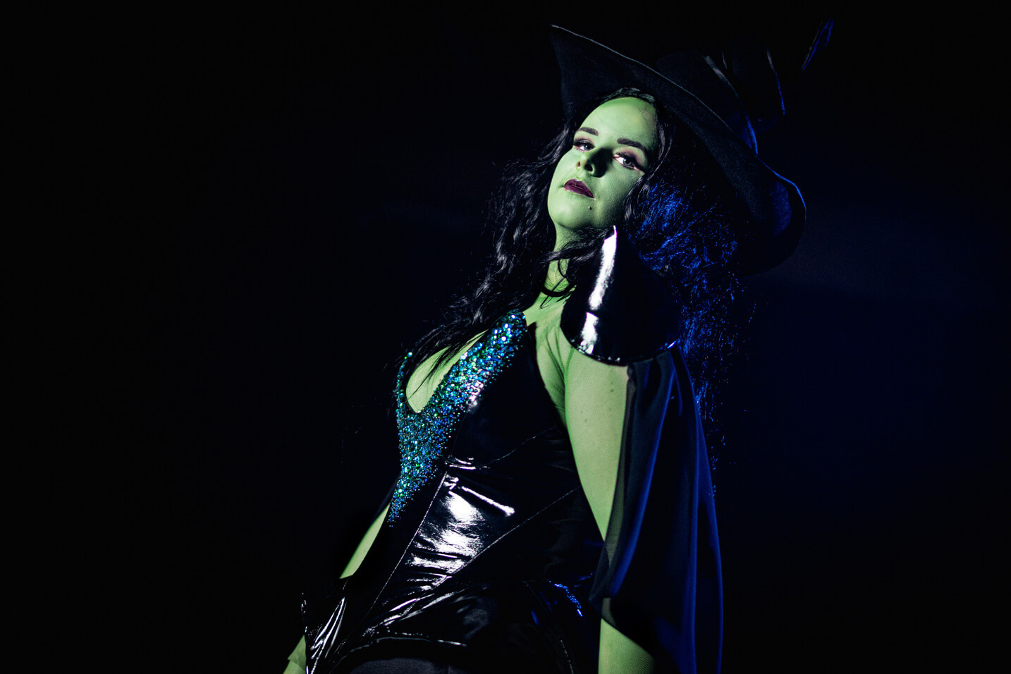 Green Witch from Wicked, wears a large oversized hat with a black sequinned corset and long skirt.