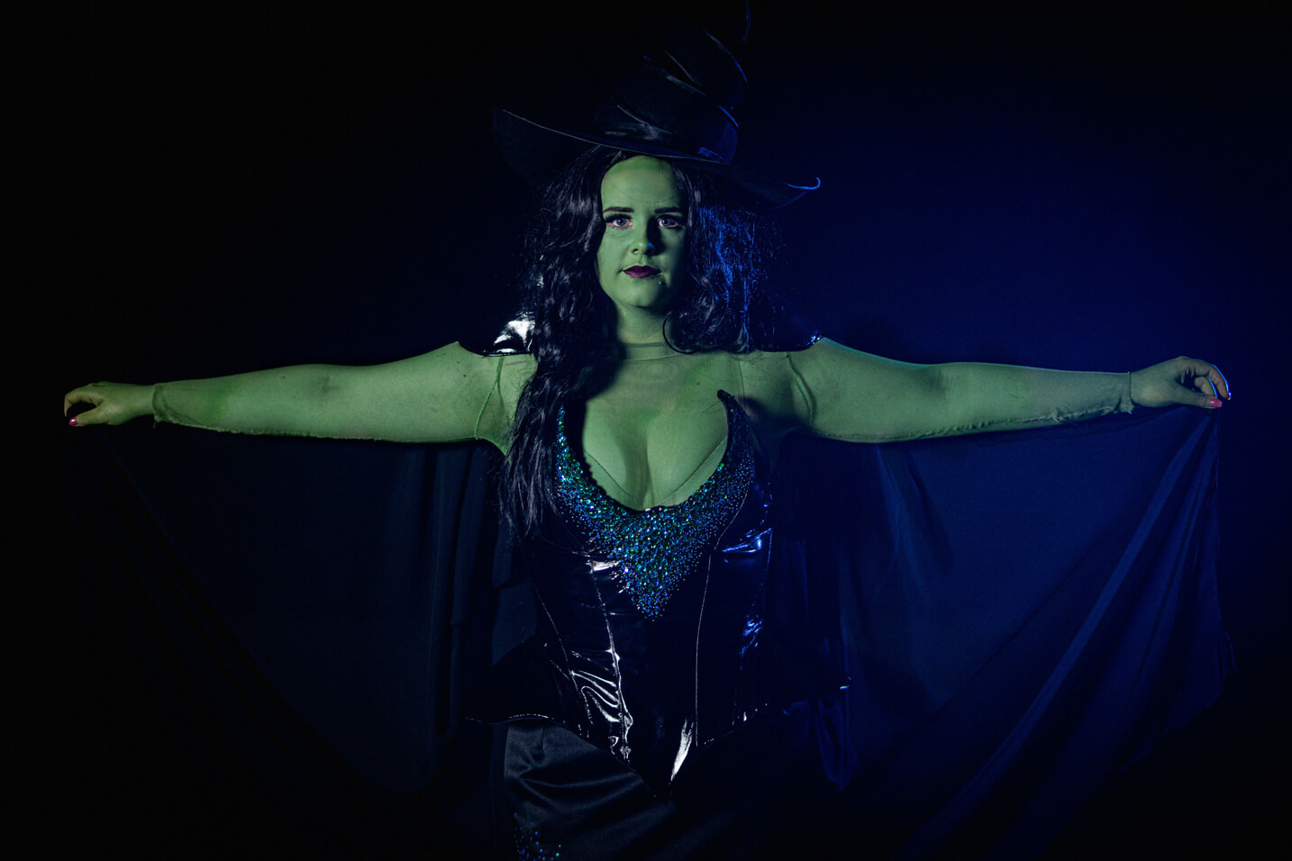 Green Witch from Wicked, wears a large oversized hat with a black sequinned corset and long skirt.