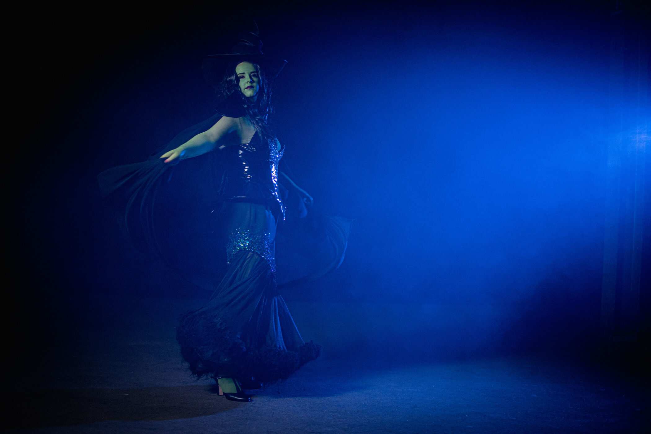 Green Witch from Wicked, wears a large oversized hat with a black sequinned corset and long skirt.