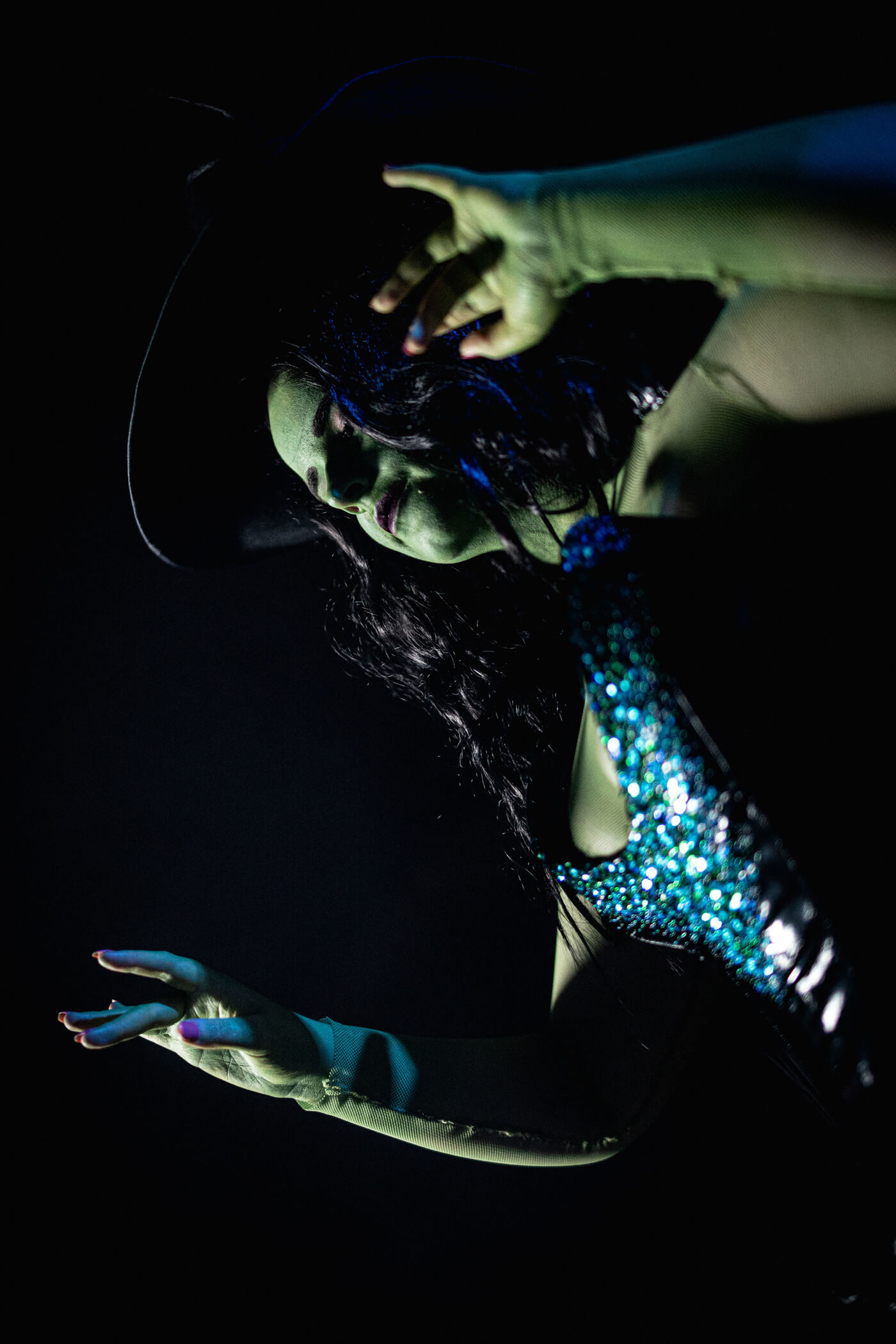 Green Witch from Wicked, wears a large oversized hat with a black sequinned corset and long skirt.