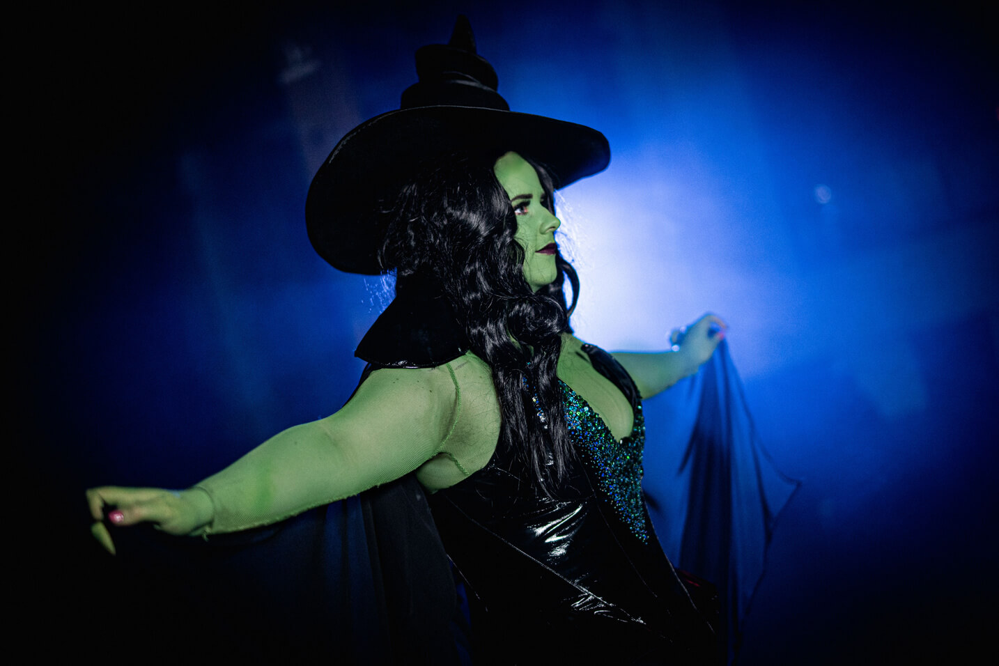 Green Witch from Wicked, wears a large oversized hat with a black sequinned corset and long skirt.