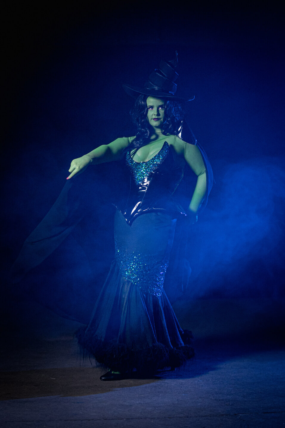 Green Witch from Wicked, wears a large oversized hat with a black sequinned corset and long skirt.