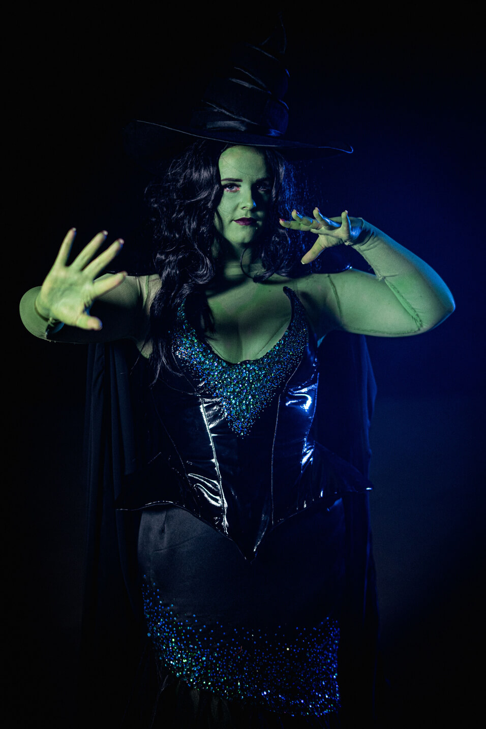 Green Witch from Wicked, wears a large oversized hat with a black sequinned corset and long skirt.