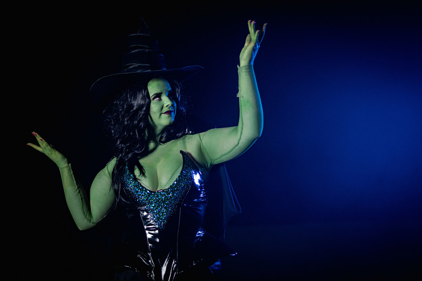 Green Witch from Wicked, wears a large oversized hat with a black sequinned corset and long skirt.