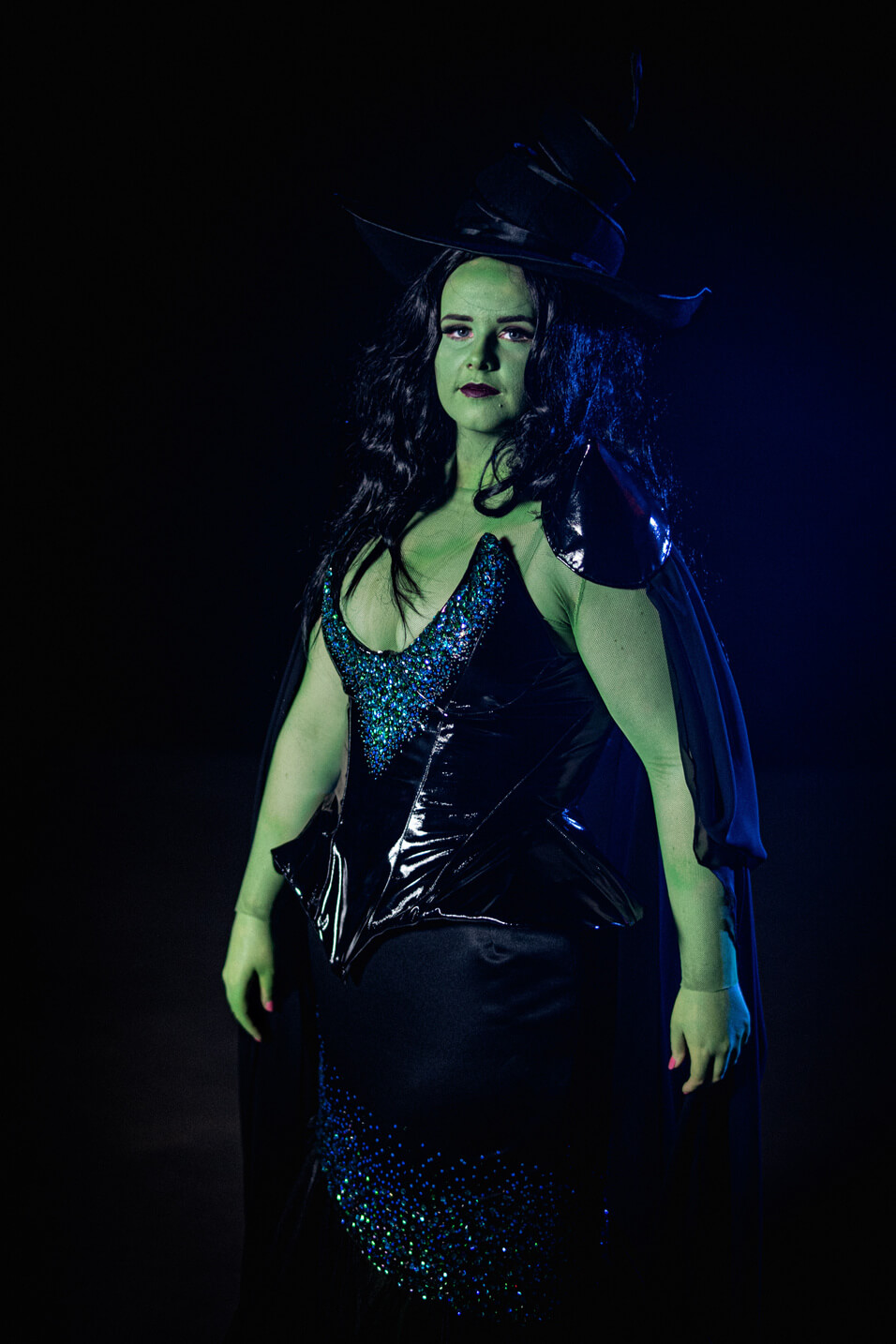 Green Witch from Wicked, wears a large oversized hat with a black sequinned corset and long skirt.