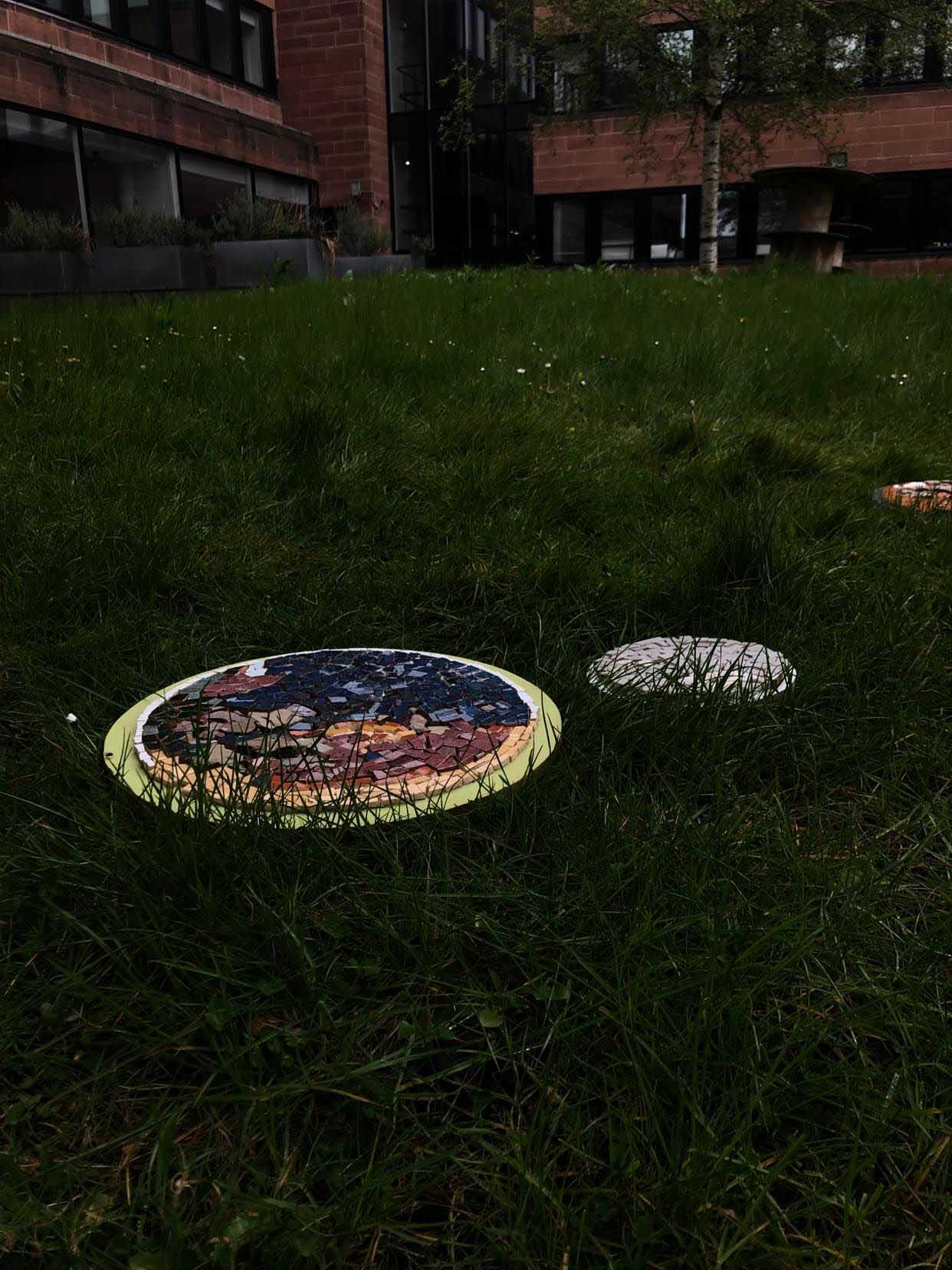 Mosaics of the Earth and Moon on grass with terracotta building in the background