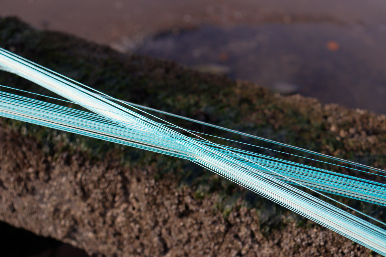 Close up of blue strands of yarn cross over to form an 'x' shape. 