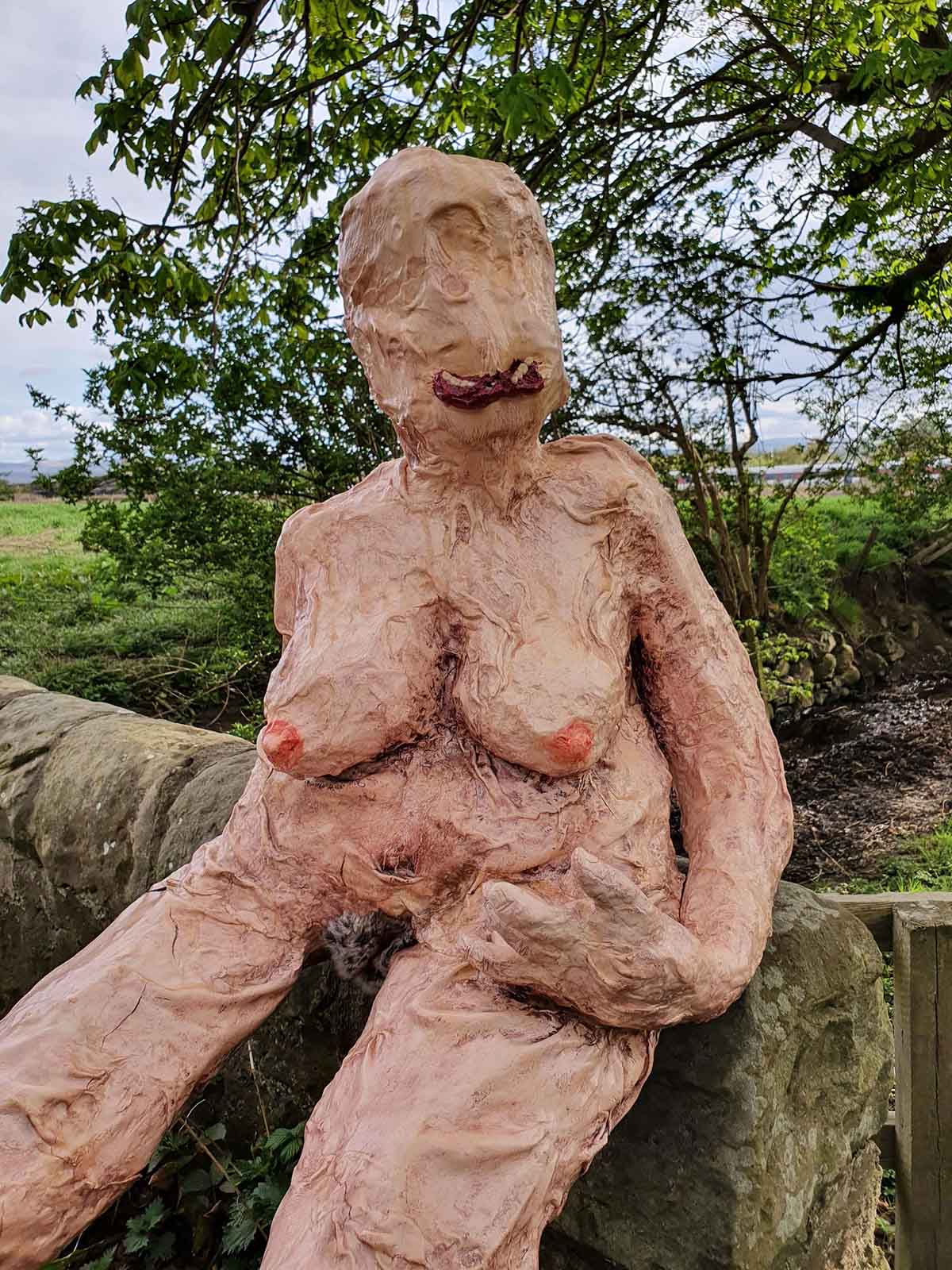 Close up of monstrous female sculpture sits on a bridge in a rural setting