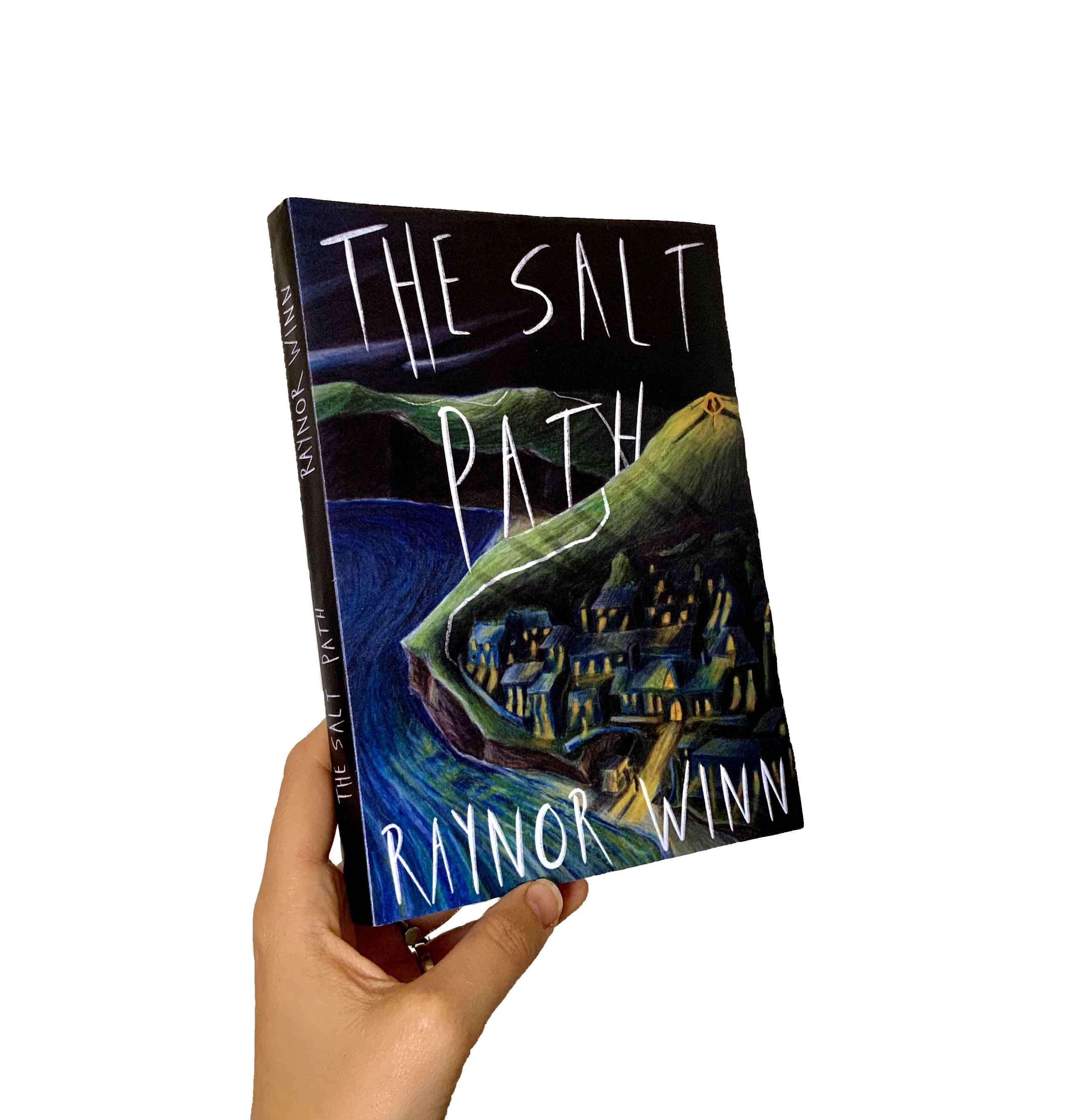 A hand holds up the Salt Path book by Raynor Winn.