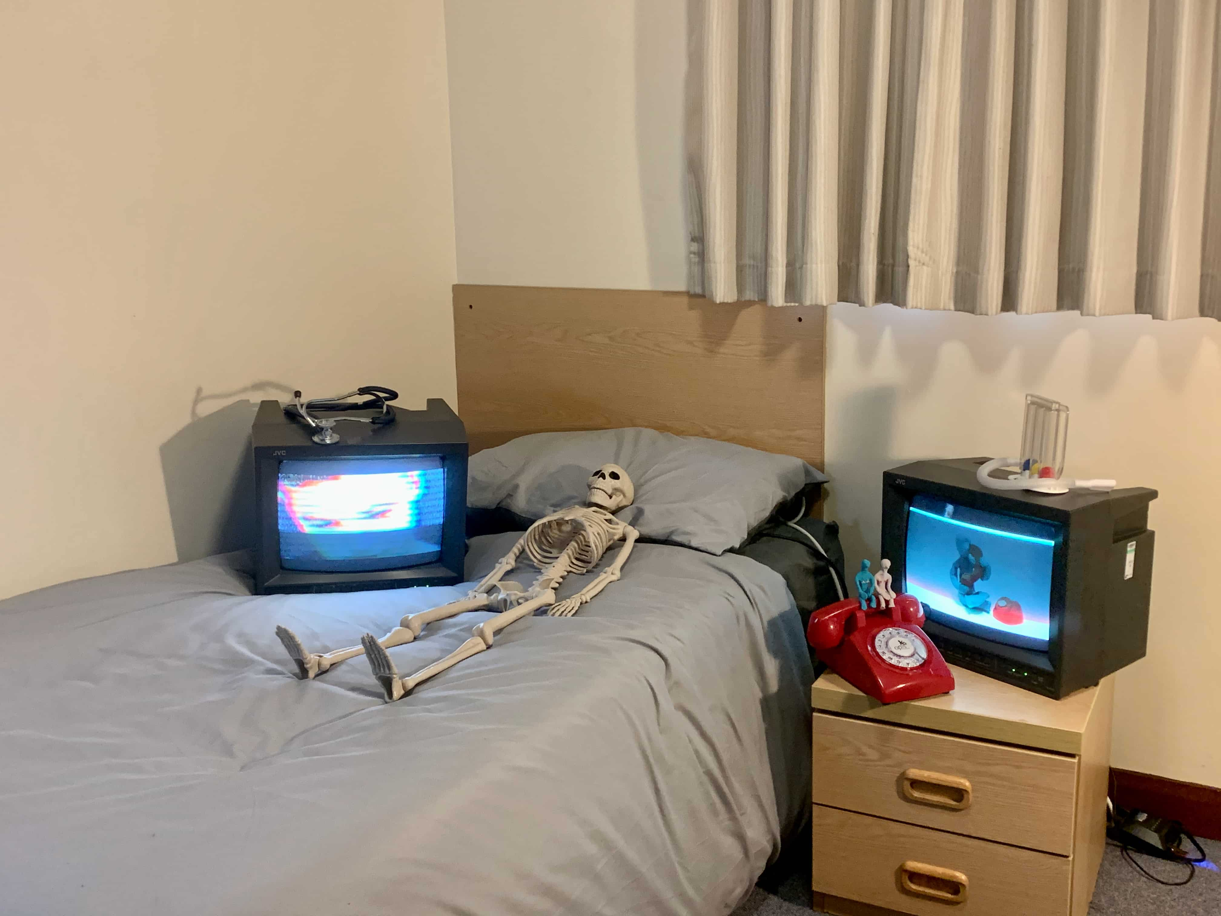 2 TVs with skeleton on bed