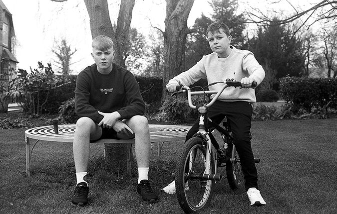 Portrait of two young boys in black and white, one is on a bike and the other is seated on a bench