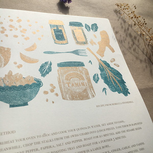 A photo of my illustrated 2022 Seasonal recipe calendar. Gives a close up look at my illustration of the ingredients to the salad, including tahini, kale, chickpeas, spices and ginger.  Risoprinted onto white paper in teal and gold. 