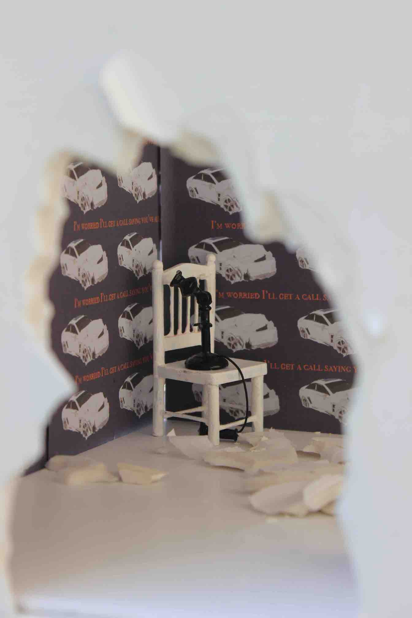 A miniature room with a hole in the wall showing a chair and a telephone