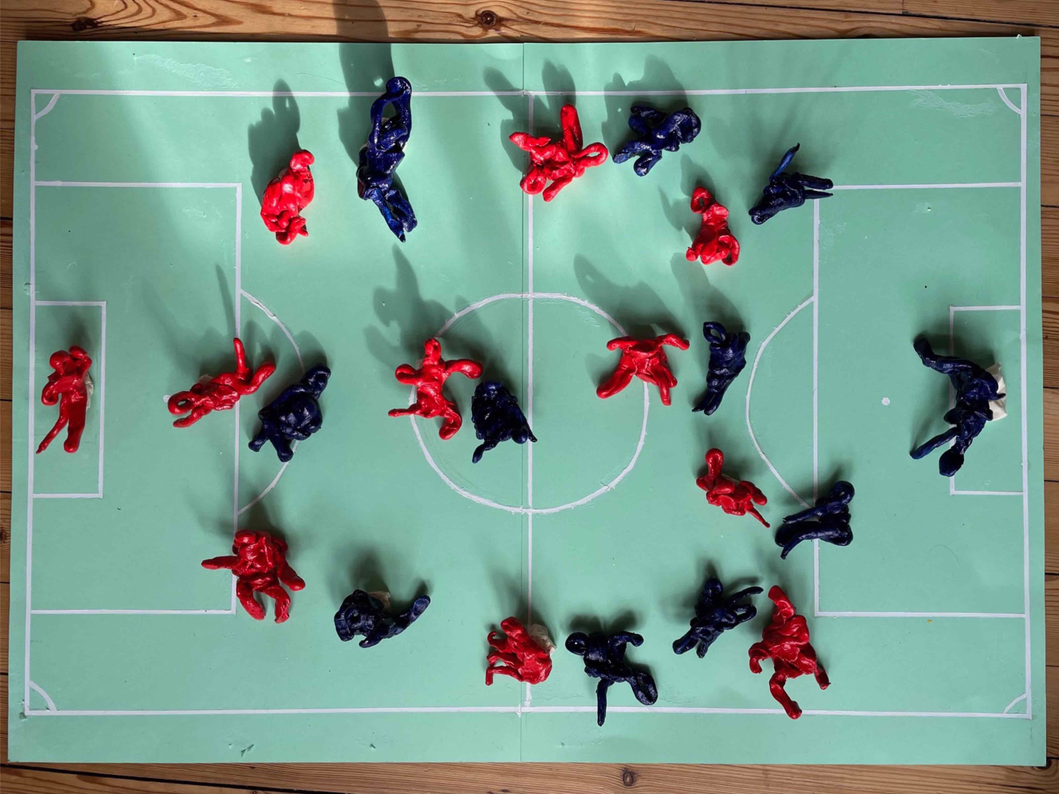 Small blue and red figures (x 22) on model football pitch.