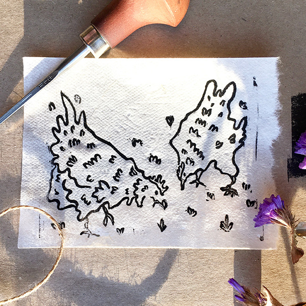 A lino printed design of two hens pecking at the grass. Black ink on white paper. 
