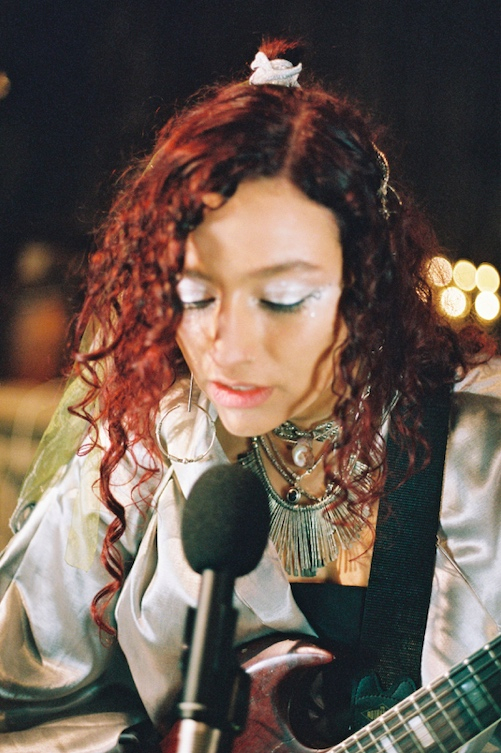 Alliyah sings close up eyes closed, playing guitar 