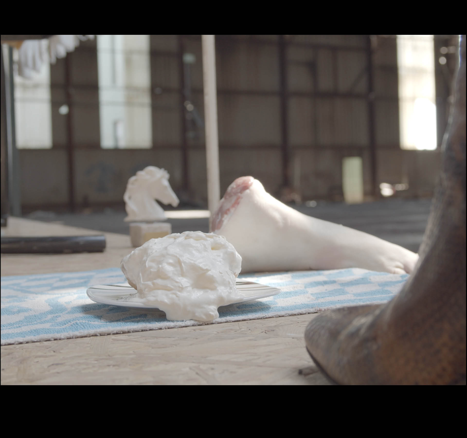 L'usine MF. Still of a filmed scenography, France, April 2021. Whipped cream, snake boot, horse statue, vertical blinds, pork trotter, tennis towel.