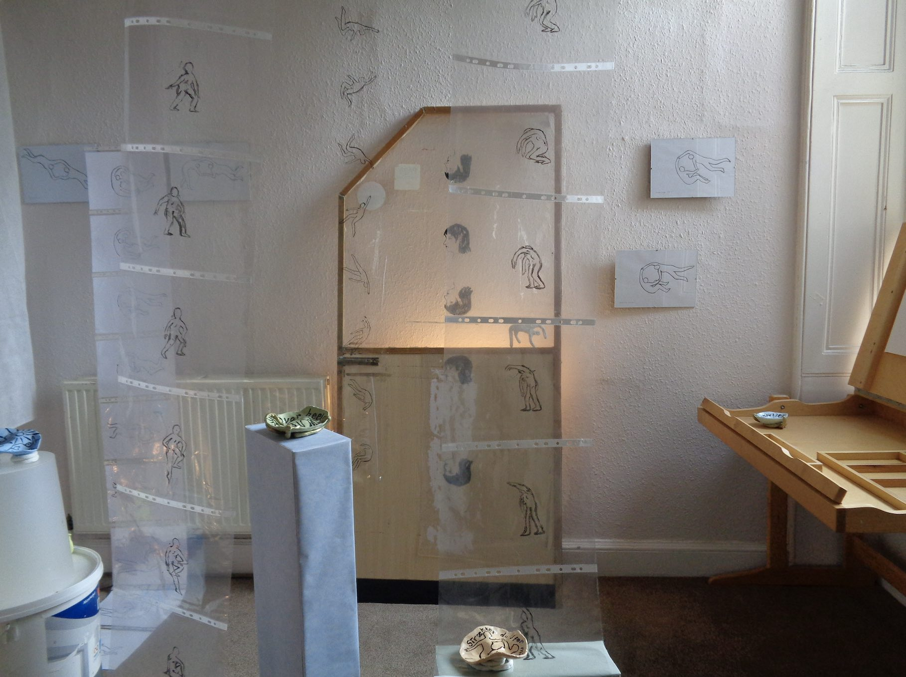 a room with ink animation frames on cellophane installed from the ceiling and plinths with small clay bowls