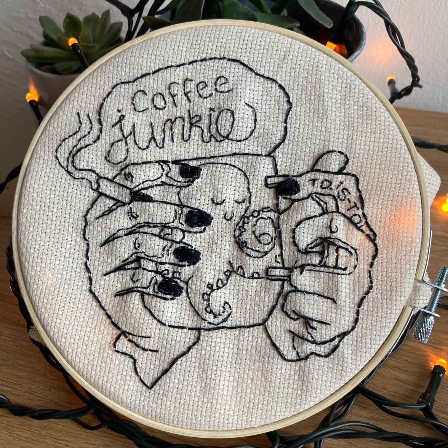 Embroidery illustration of hands holding a cup and a cigarette. Text says "coffee junkie"