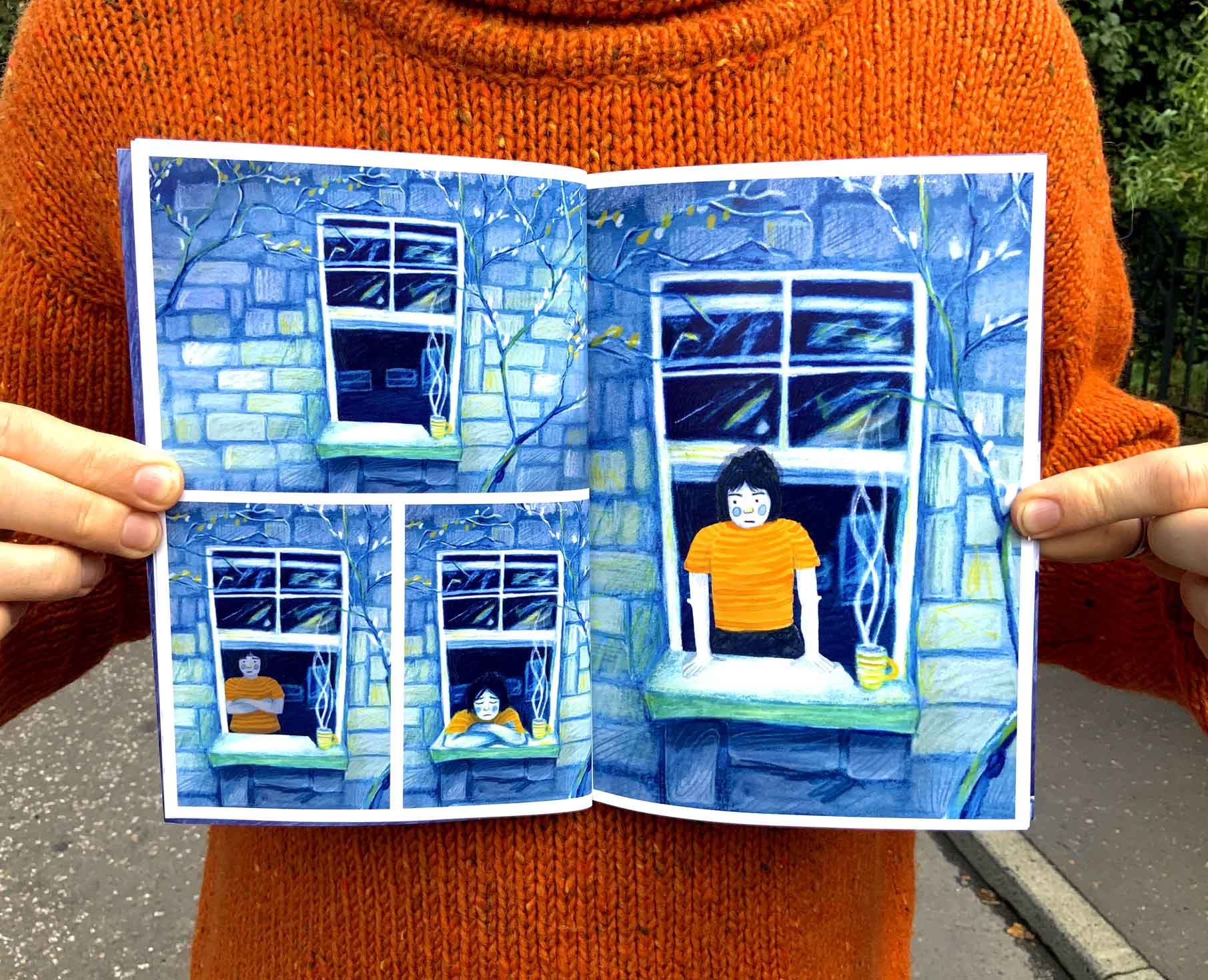 Someone holds an open book showing images of a window. Someone is emerging from it.