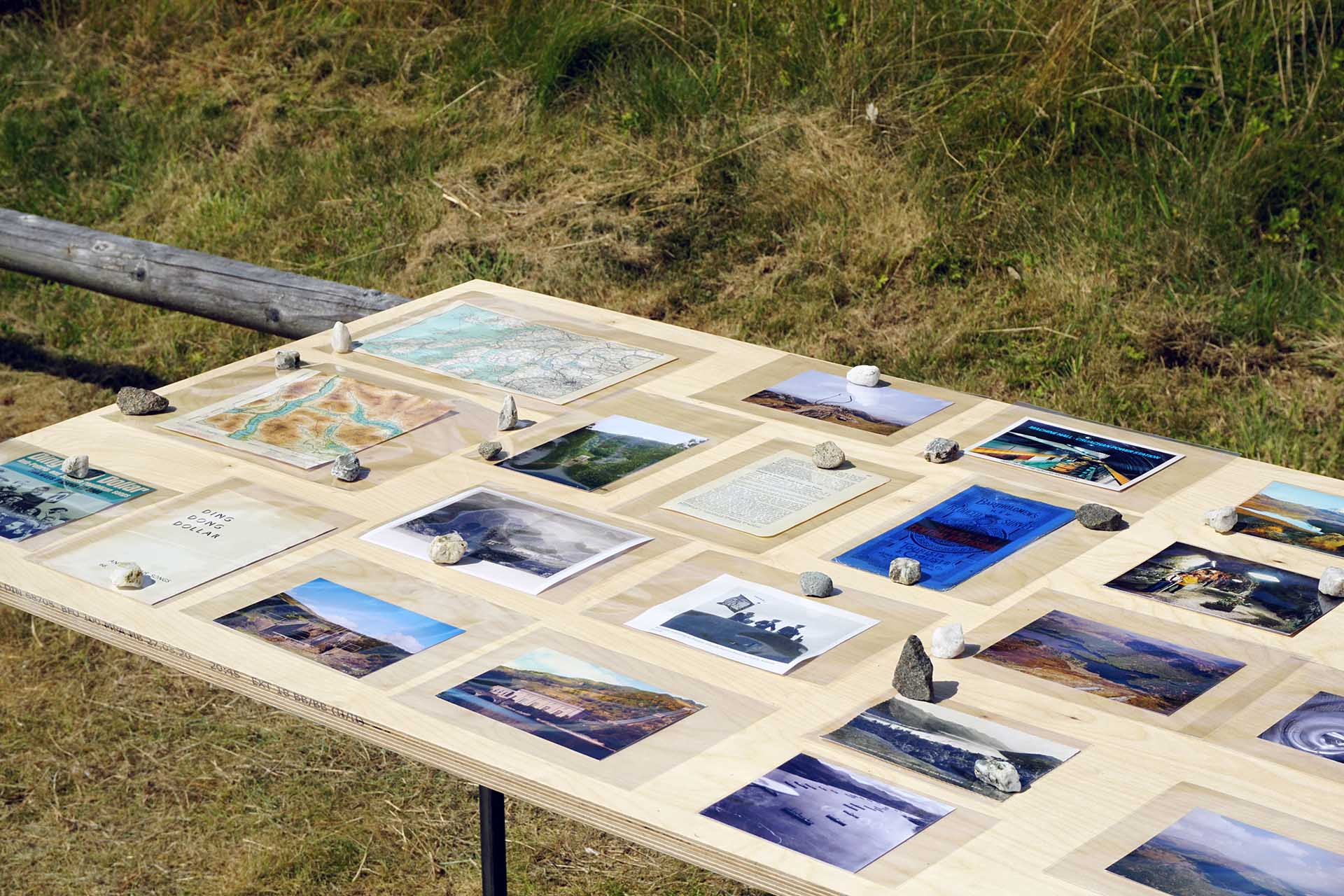 A view of collected archival materials placed on a the birch ply table, these are a mix of postcards, news clippings, personal photography, information sheets and maps