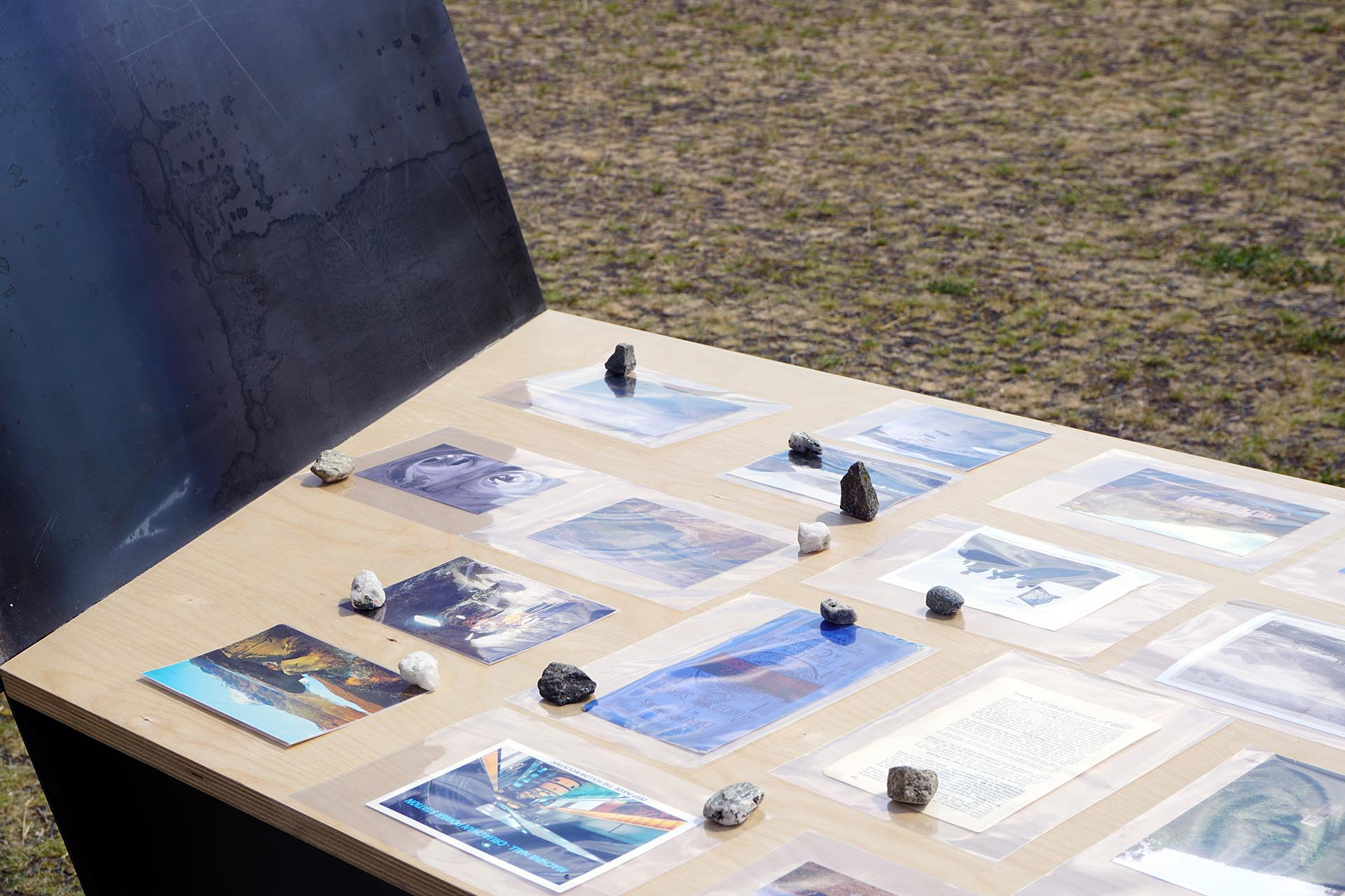 Collected archival materials displayed on birch ply table with hot rolled steel acoustic deflector sliced through it in this photo you can see the blue of the steel and how it cleanly slices an angle through the table  