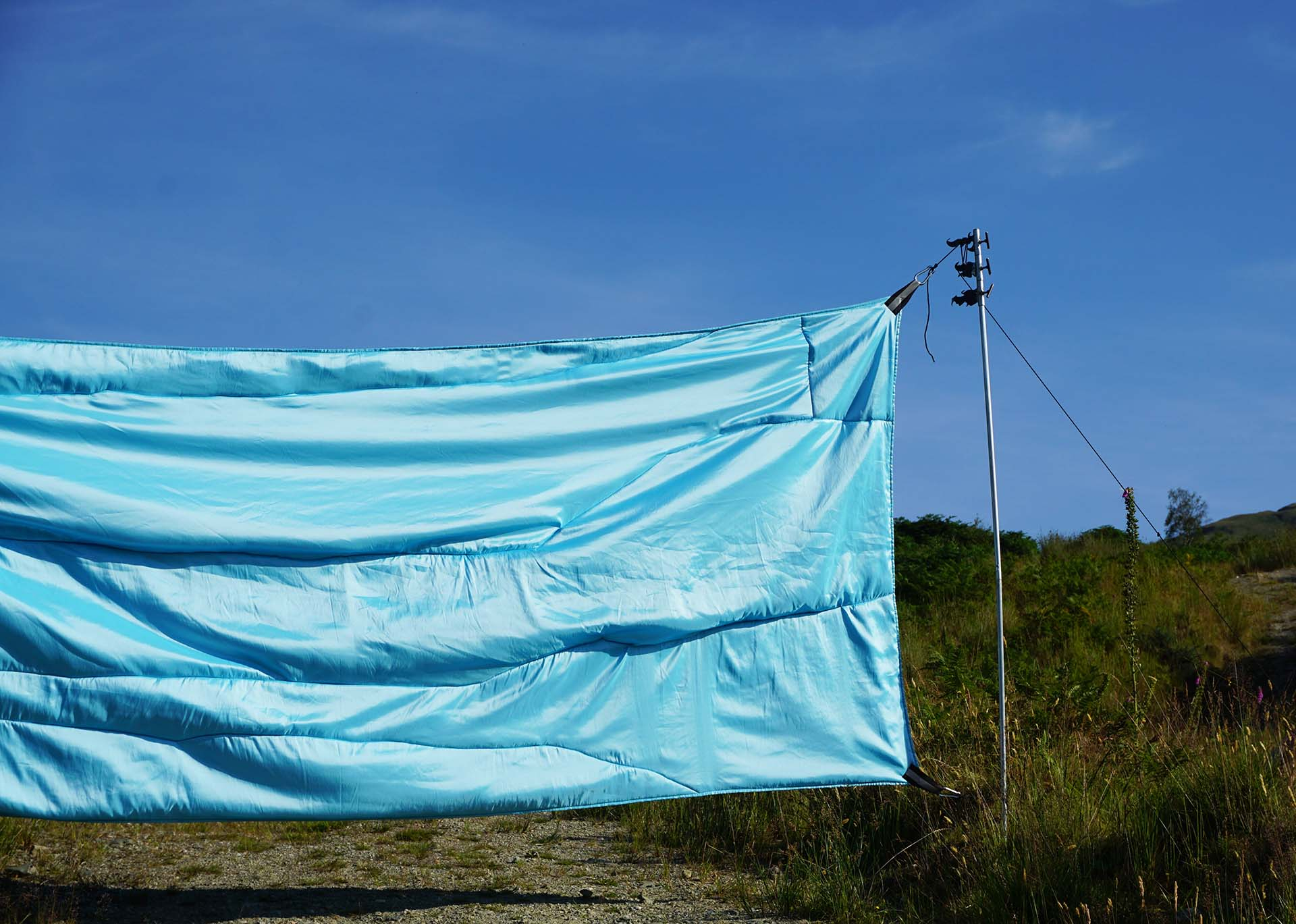 a close up view of baby blue two toned taffeta (1.5 m x 4.5 m) stretch across a path situated half way up a mountain in this image you can see the hanging rods created for this work that resemble celtic spears