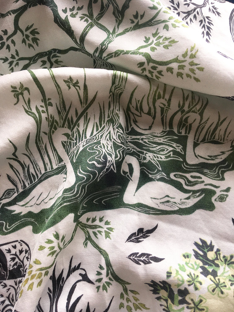 Close-up image of fabric with folds. On the fabric are images of swans, leaves, feathers and flowers.