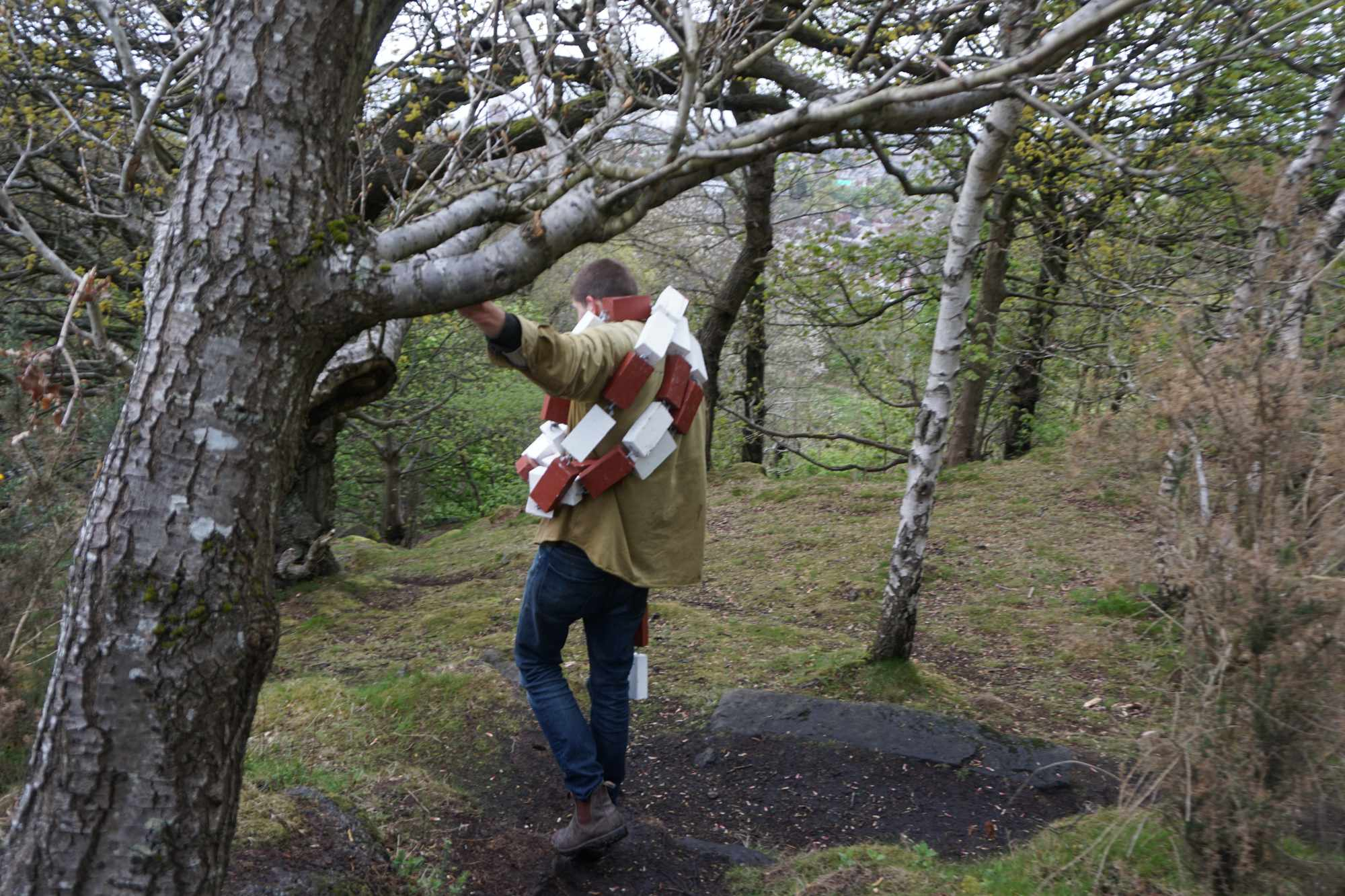 A long wooden chain wrapped about the artist as it is transported through the woods.