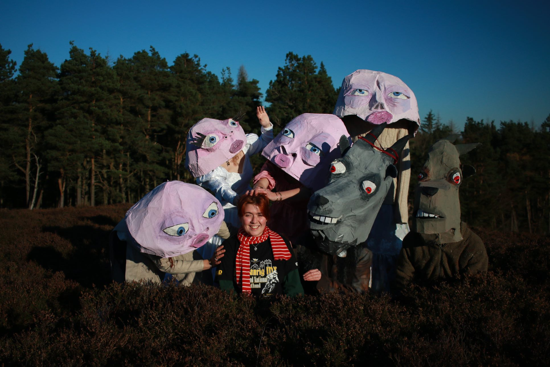 Artist surrounded by people in papier-mâché masks in a field.