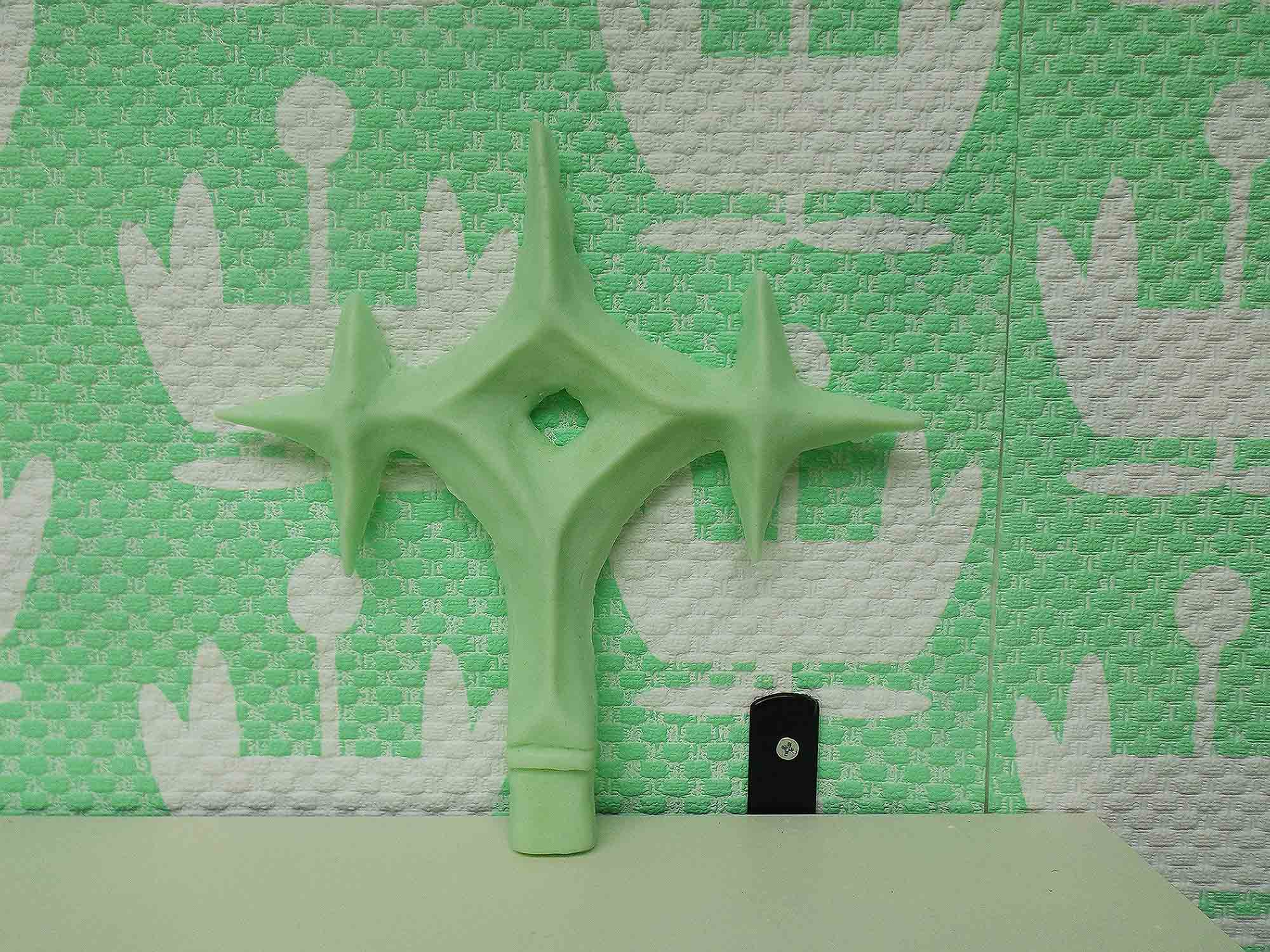 pastel green soap in the shape of a cross on white shelf with green floral wallpaper behind