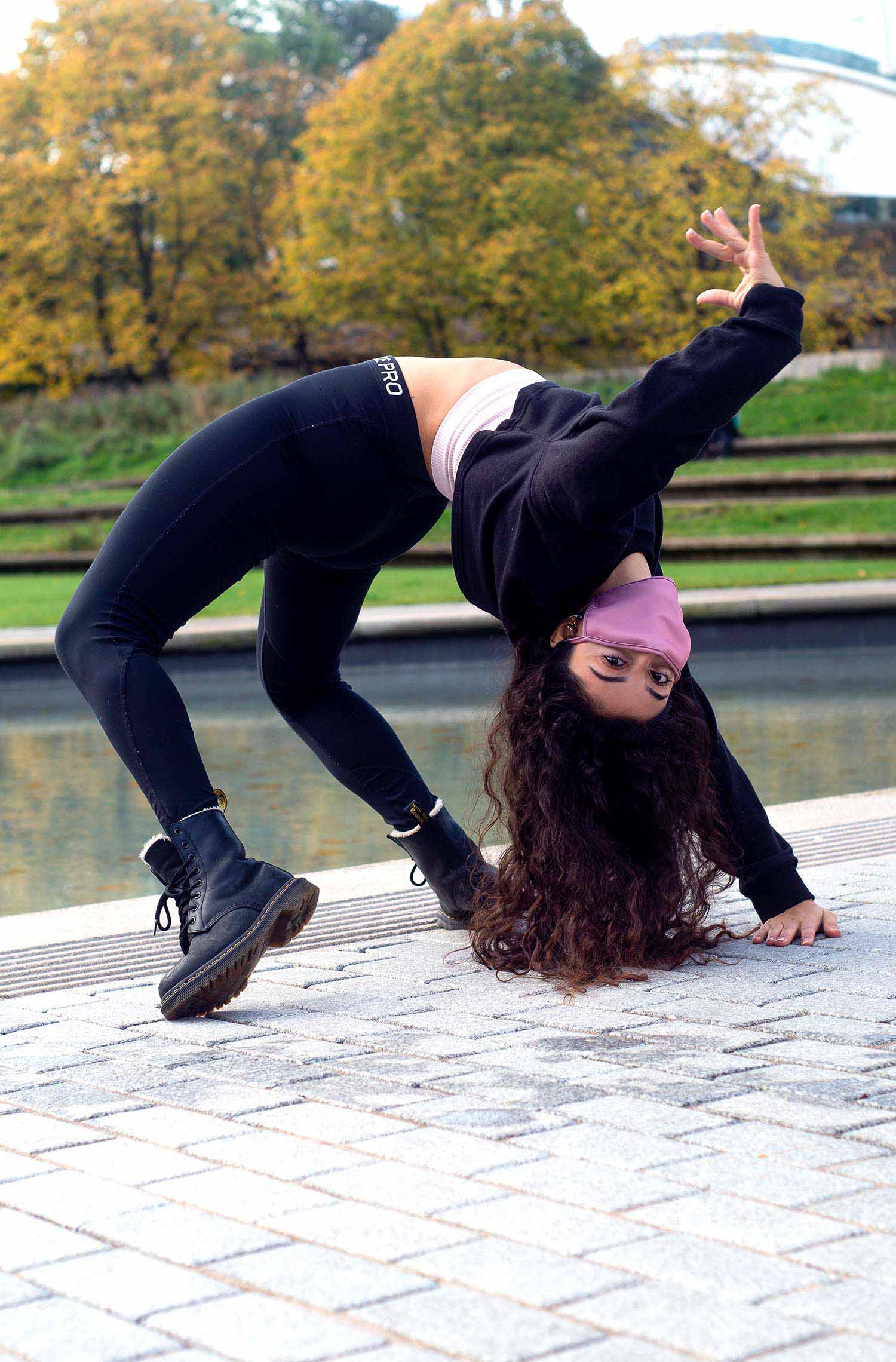 A dancer bent over in a bridge in front of trees and water.