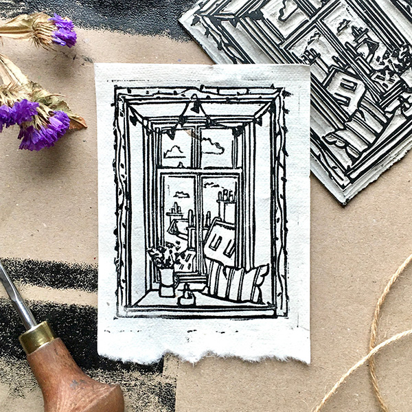A6 lino print of a window seat with a cushion, vase of flowers, and candle. Hand pressed onto rice paper using a metal spoon