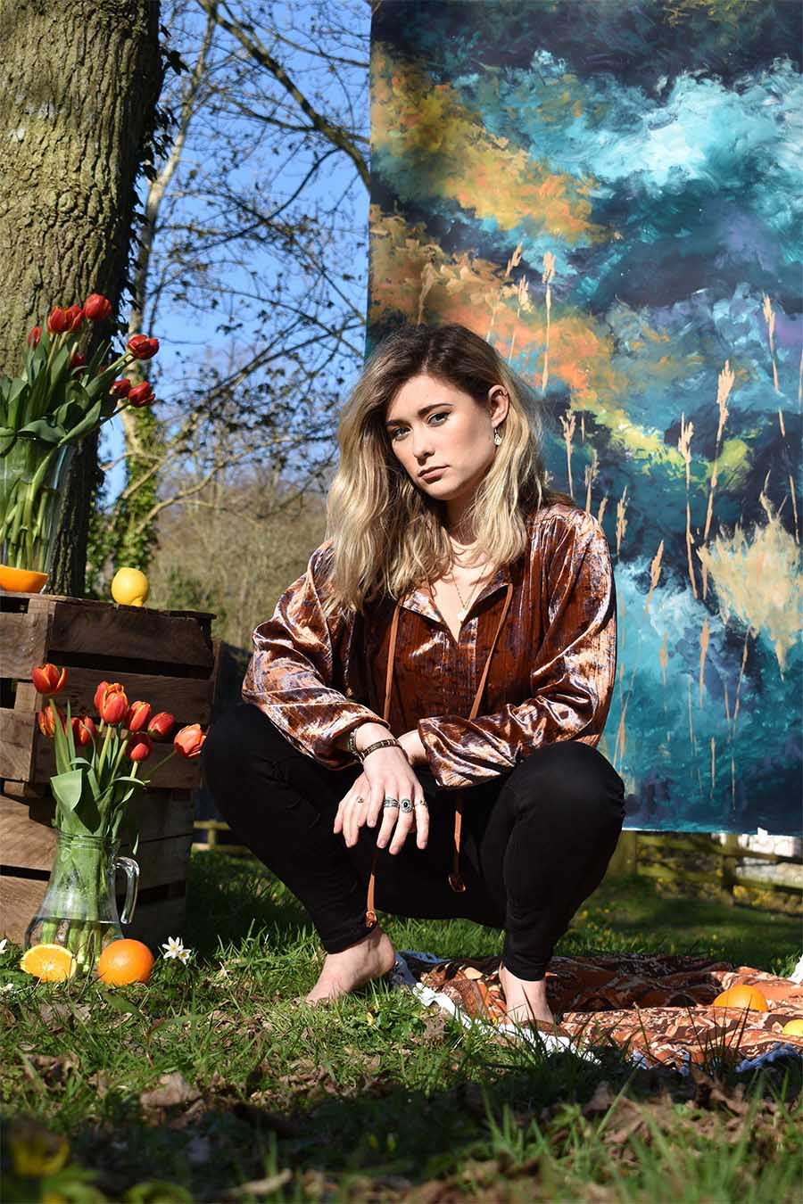 Model posing in a crouched position in front of a painted backdrop. She is surrounded by oranges and tulips.